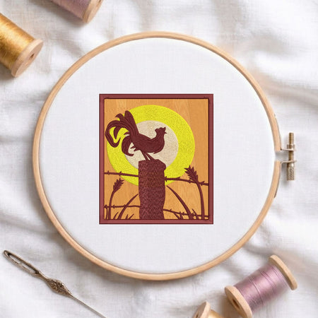 Rooster on a fence machine embroidery design displayed in a wooden hoop on white fabric with thread spools and a needle   