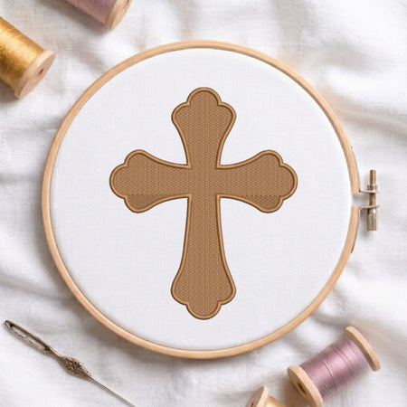 Light brown scalloped cross with a darker brown outline embroidered on white fabric inside a wooden hoop.