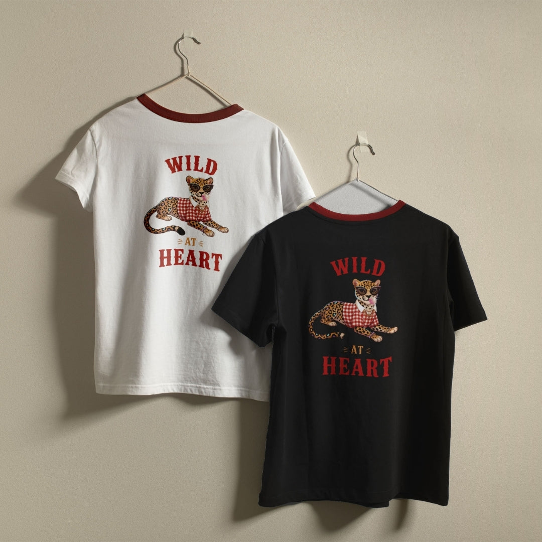 White and bright green t-shirts hanging on a wall, both displaying the quirky "Wild At Heart" leopard design printed on the back.