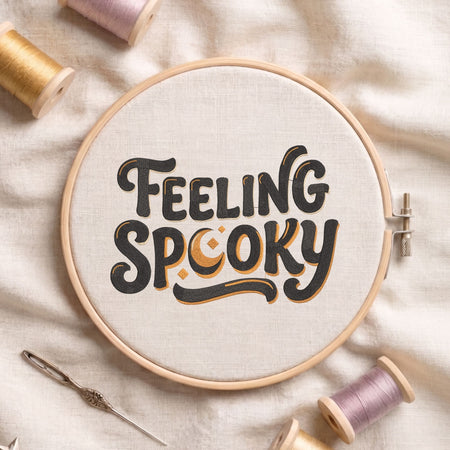 Feeling Spooky" retro lettering machine embroidery design featuring dark charcoal text with gold accents, displayed inside a round wooden hoop on white linen fabric alongside thread spools and a needle.

