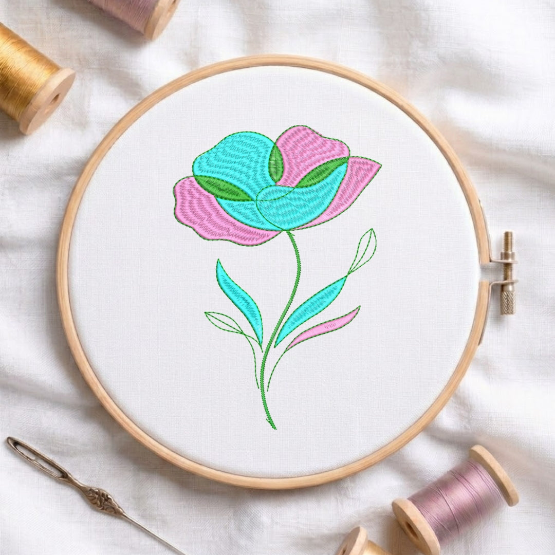 A floral embroidery design in a wooden hoop, featuring pink and turquoise petals with green leaves on a white fabric background, surrounded by spools of thread and a needle.