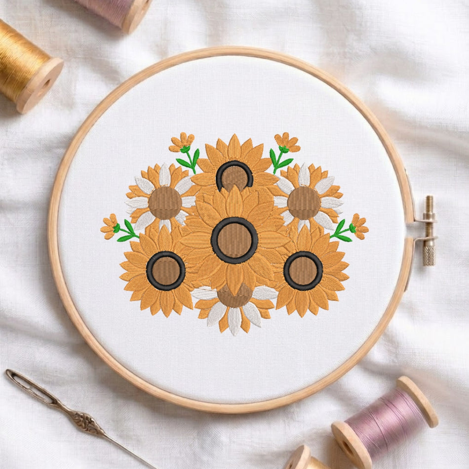 A circular embroidery hoop holding white fabric with a floral sunflower design in yellow, brown, black, and green thread, styled on a white fabric background with spools of thread and a needle.
