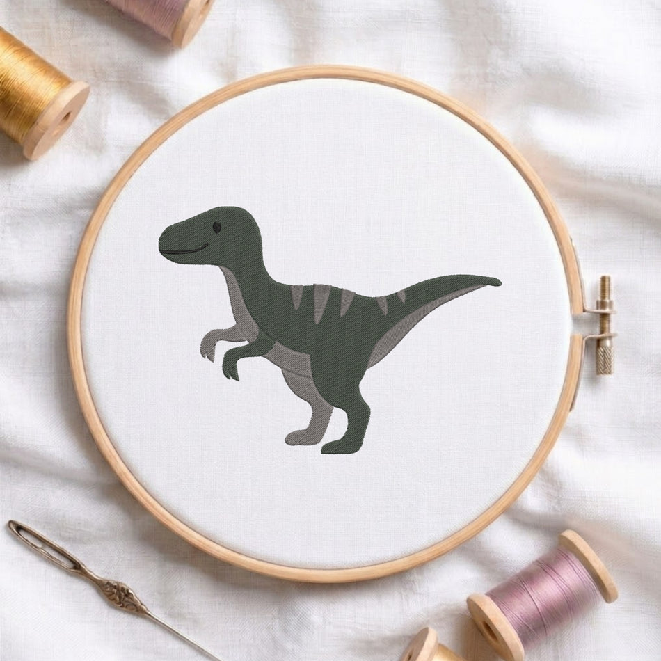 A wooden embroidery hoop holds white fabric with a dark green cartoon dinosaur design. The hoop is styled on a white fabric background with spools of thread and a needle around it.