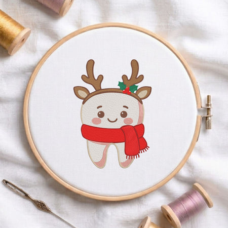 Cute smiling tooth wearing reindeer antlers and a cozy red scarf Christmas dental machine embroidery design shown in a wooden embroidery hoop on white fabric with thread spools and a needle