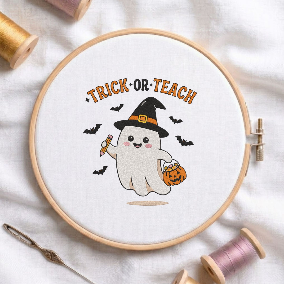 Trick or Teach" cute teacher ghost wearing a witch hat, holding a pencil and pumpkin treat bag machine embroidery design shown in a wooden embroidery hoop on white fabric with thread spools and a needle   