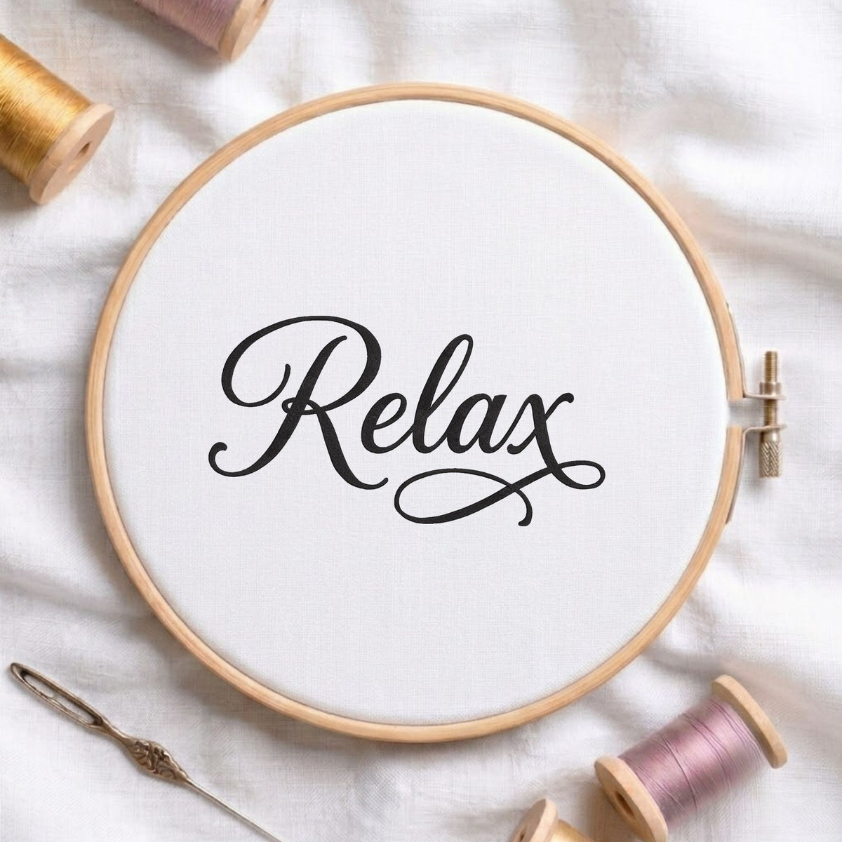 "Relax" script typography machine embroidery design displayed in a wooden hoop on white fabric with thread spools and a needle