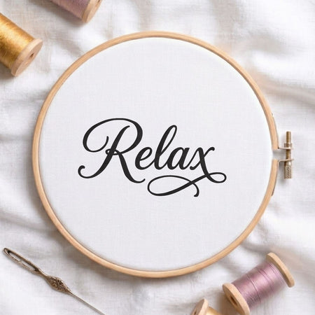 "Relax" script typography machine embroidery design displayed in a wooden hoop on white fabric with thread spools and a needle