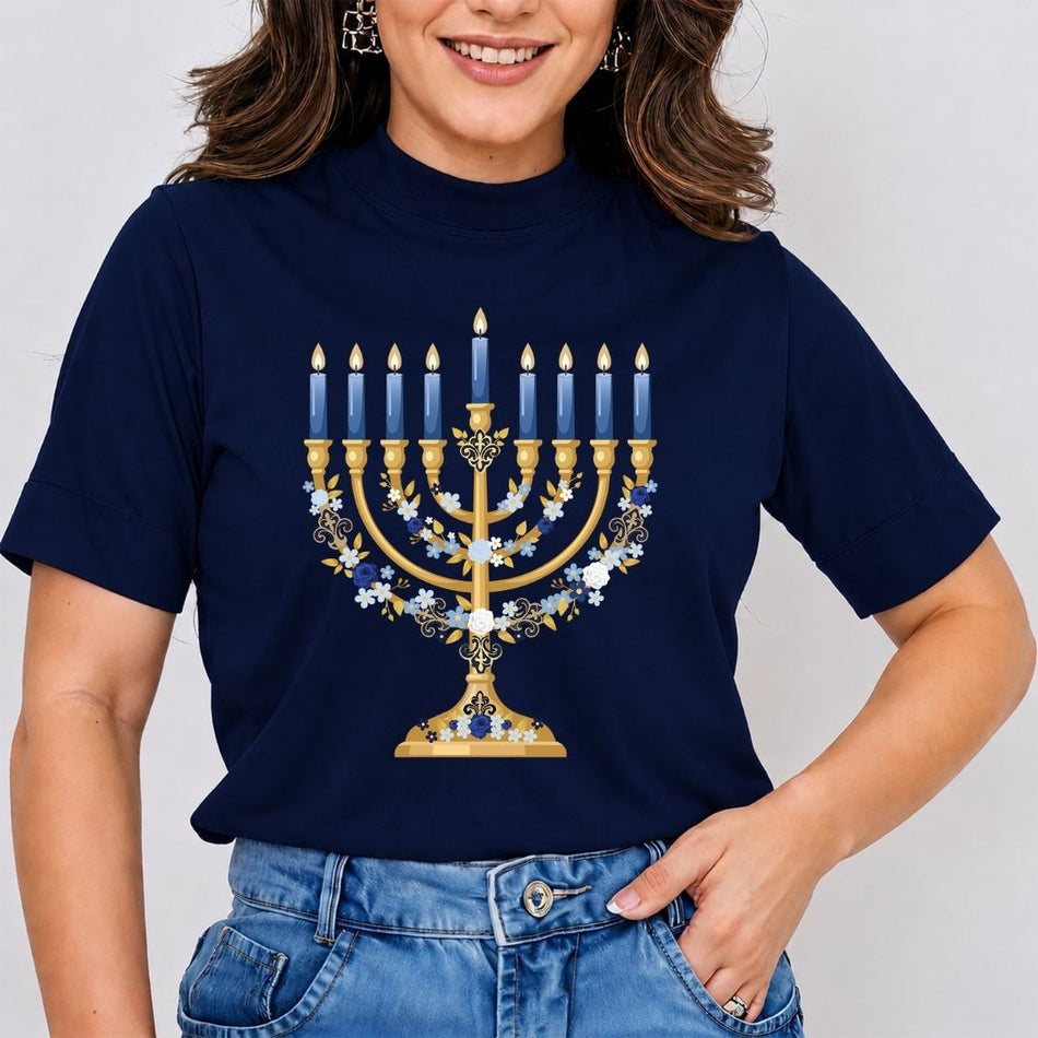 A woman wearing a navy blue mock-neck t-shirt with a gold Hanukkah menorah graphic decorated with blue and white candles and flowers, paired with blue jeans.