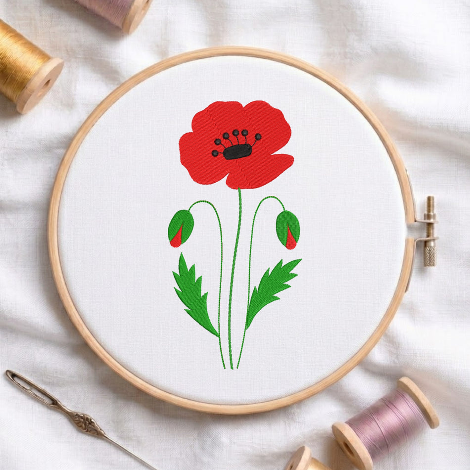 Bright red poppy wildflower with green stems and buds embroidered inside a round wooden hoop with thread spools.