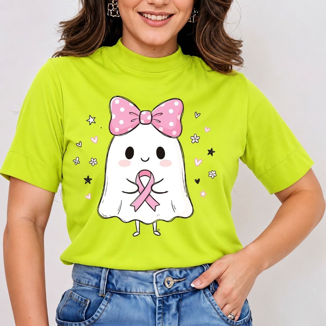 A woman wearing a bright lime green mock-neck t-shirt with a cute cartoon ghost graphic holding a pink breast cancer awareness ribbon, paired with blue jeans.