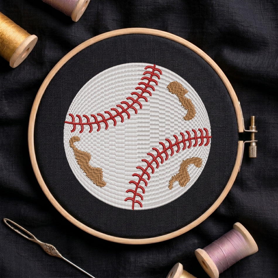 A circular embroidery hoop holds a baseball-themed cross-stitch design on black fabric, surrounded by spools of thread and a needle.