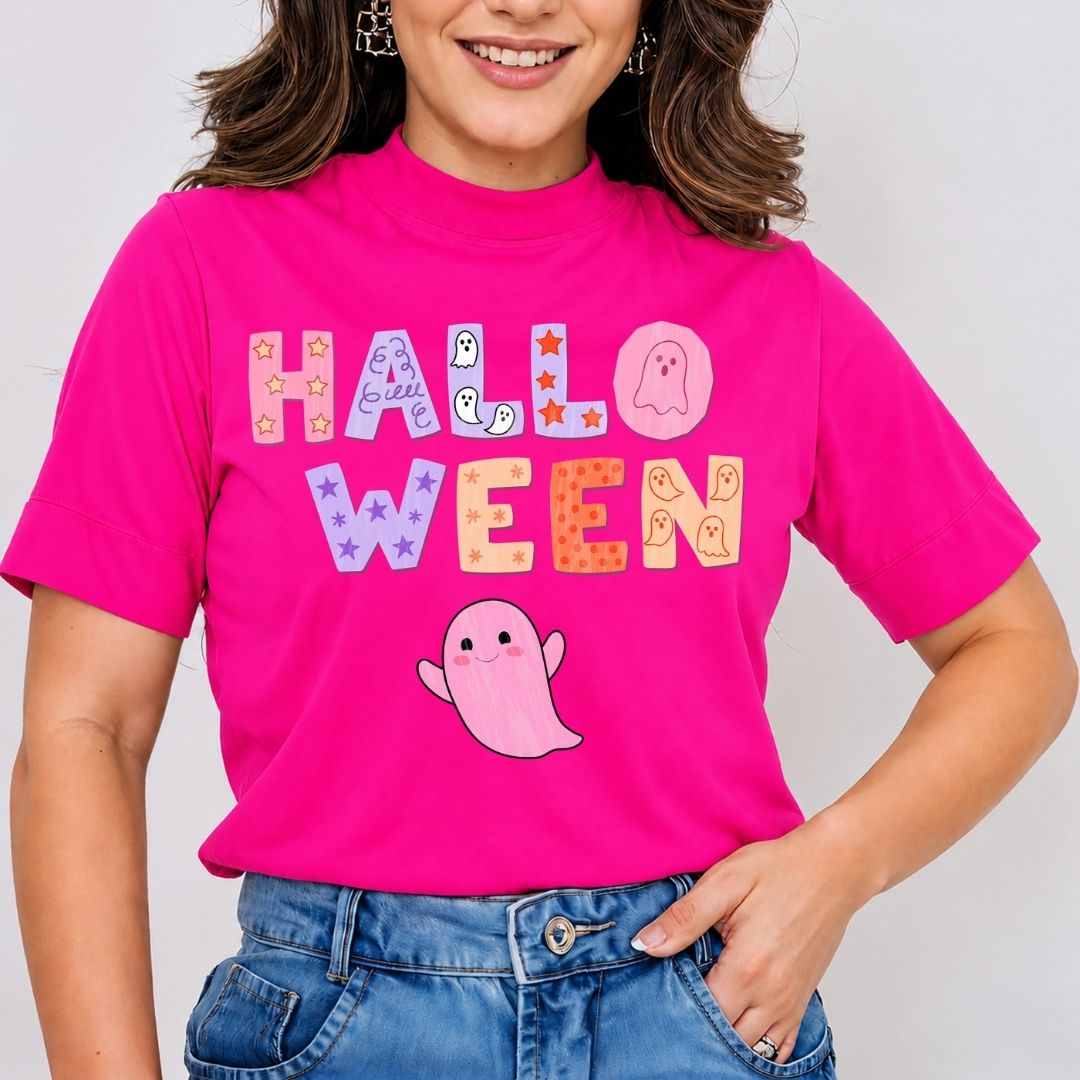 A woman wearing a bright pink mock-neck t-shirt with a colorful 'HALLOWEEN' graphic and a cute pink ghost, paired with blue jeans.