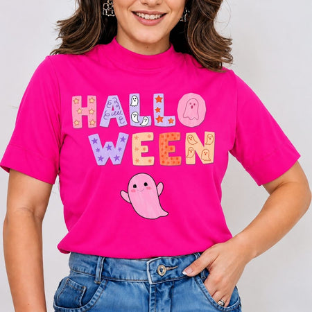 A woman wearing a bright pink mock-neck t-shirt with a colorful 'HALLOWEEN' graphic and a cute pink ghost, paired with blue jeans.