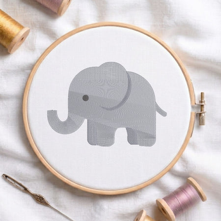 A circular embroidery hoop holding white fabric with a gray elephant design, surrounded by spools of thread and a needle on a white fabric background.
