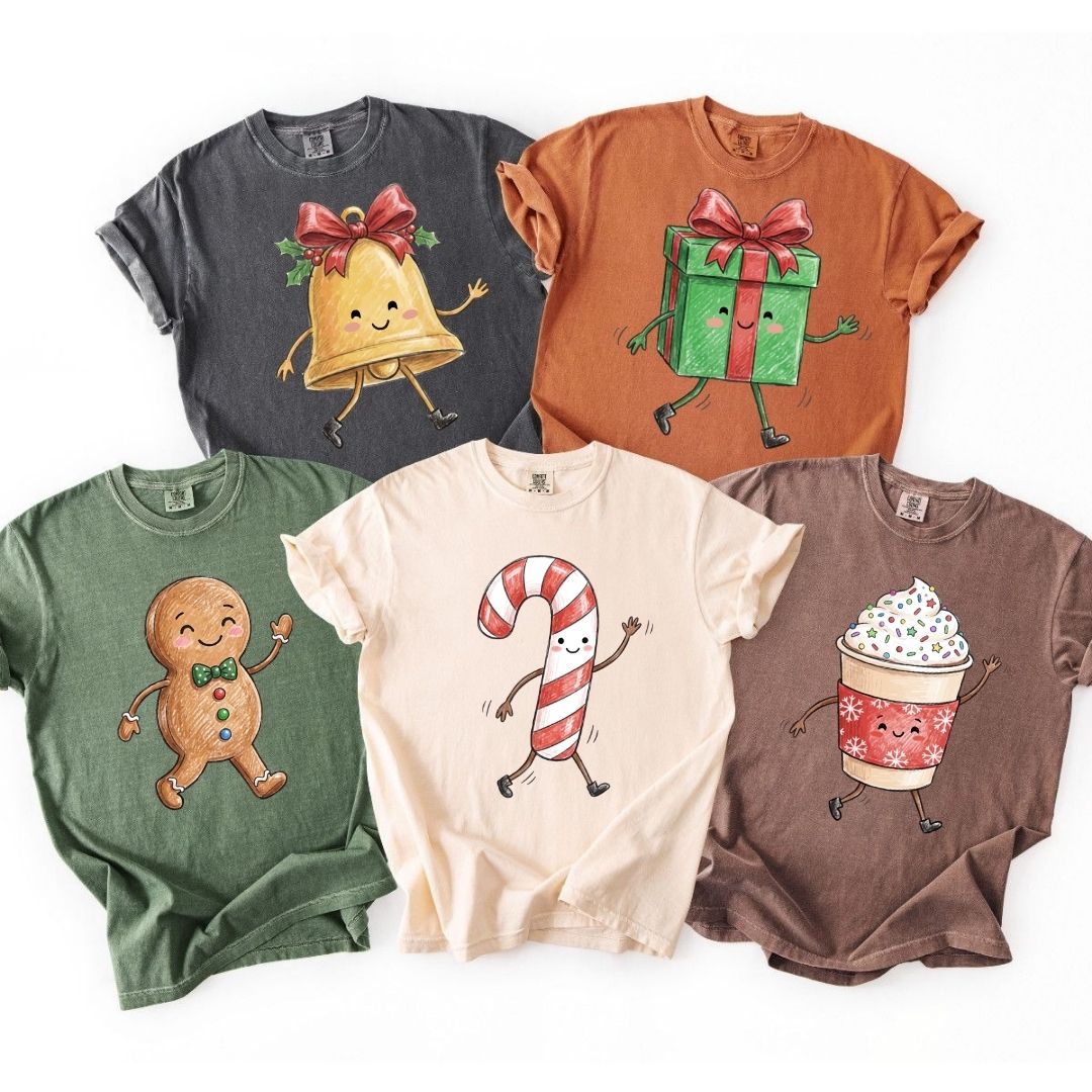 Five short-sleeve crewneck t-shirts in different colors, each featuring a different cute Christmas-themed cartoon graphic including a bell, gift box, gingerbread man, candy cane, and hot cocoa cup.
