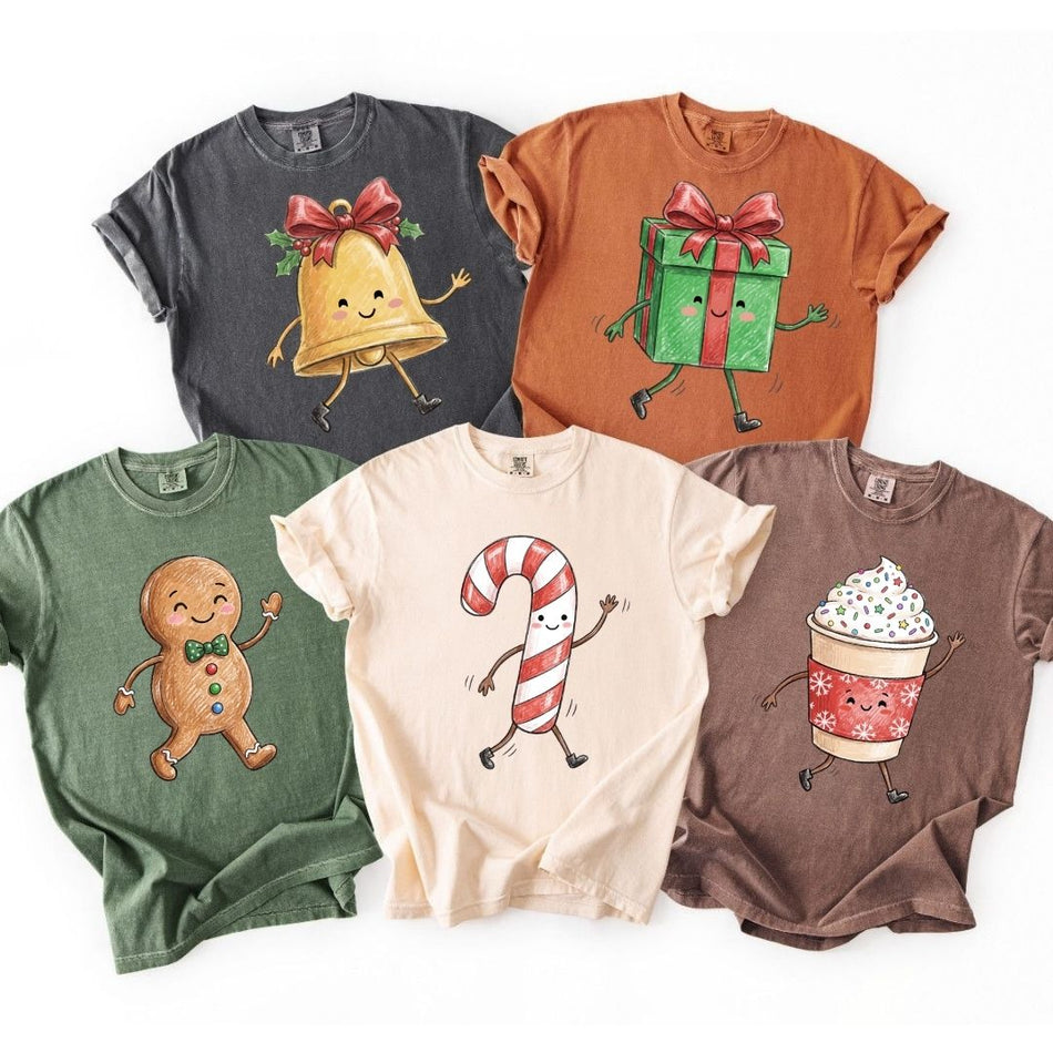 Five short-sleeve crewneck t-shirts in different colors, each featuring a different cute Christmas-themed cartoon graphic including a bell, gift box, gingerbread man, candy cane, and hot cocoa cup.