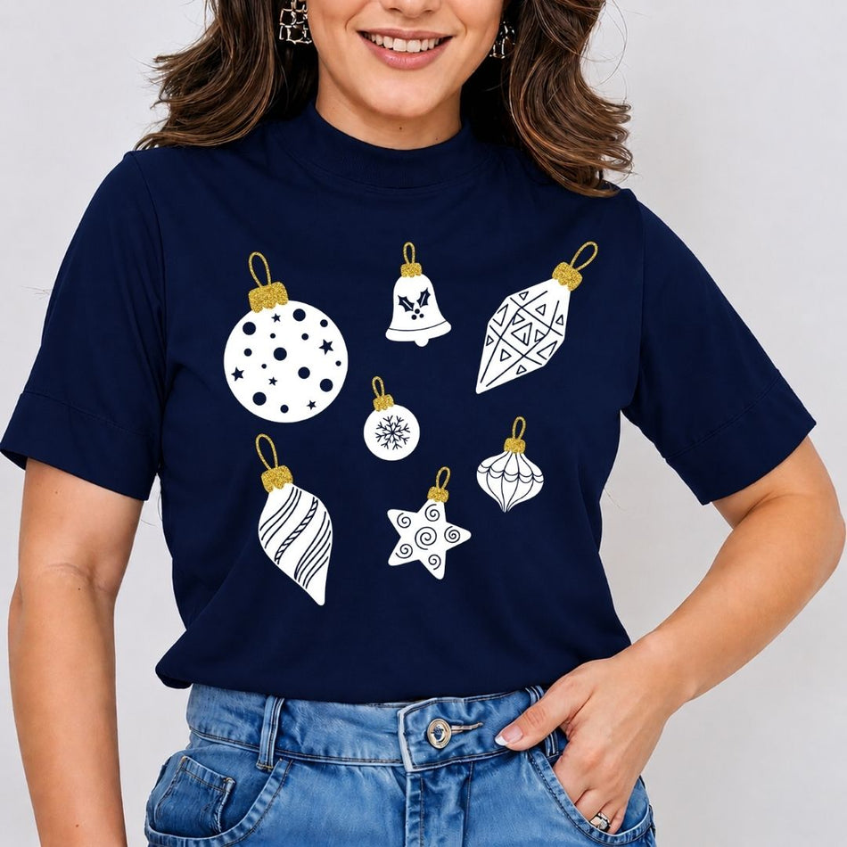 A woman wearing a navy blue mock-neck t-shirt with a graphic print of six white Christmas ornaments, paired with blue jeans, against a light gray background.