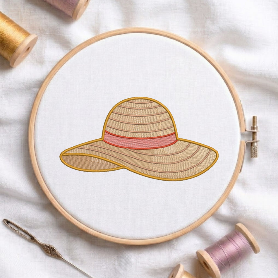 A circular embroidery hoop holds white fabric with a stitched sun hat design in beige, pink, and gold thread. A needle and spools of thread are arranged around it on a white fabric background.