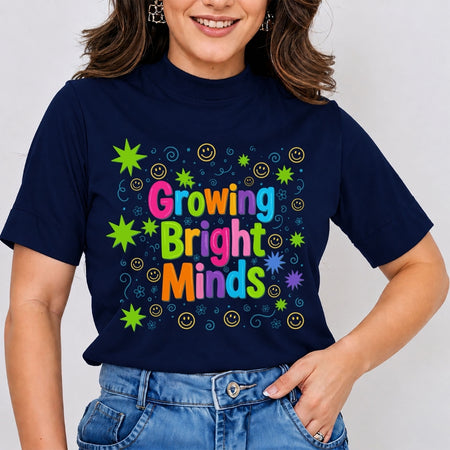 A woman wearing a navy blue t-shirt with a colorful graphic that reads 'Growing Bright Minds' in rainbow letters, surrounded by smiley faces, stars, and swirls, paired with blue jeans.