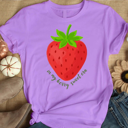 Purple t-shirt with a strawberry graphic and text on a textured surface.