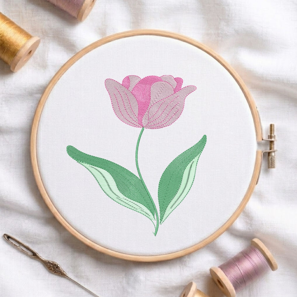 A round embroidery hoop holding white fabric with a stitched pink tulip and green leaves, surrounded by spools of thread and a needle on a white fabric background.