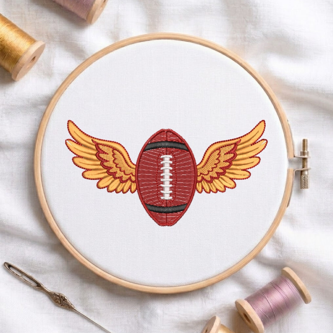Embroidery hoop with a red football design on white fabric, surrounded by spools of thread.
