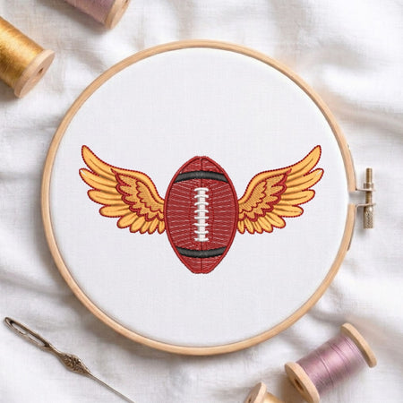 Embroidery hoop with a red football design on white fabric, surrounded by spools of thread.