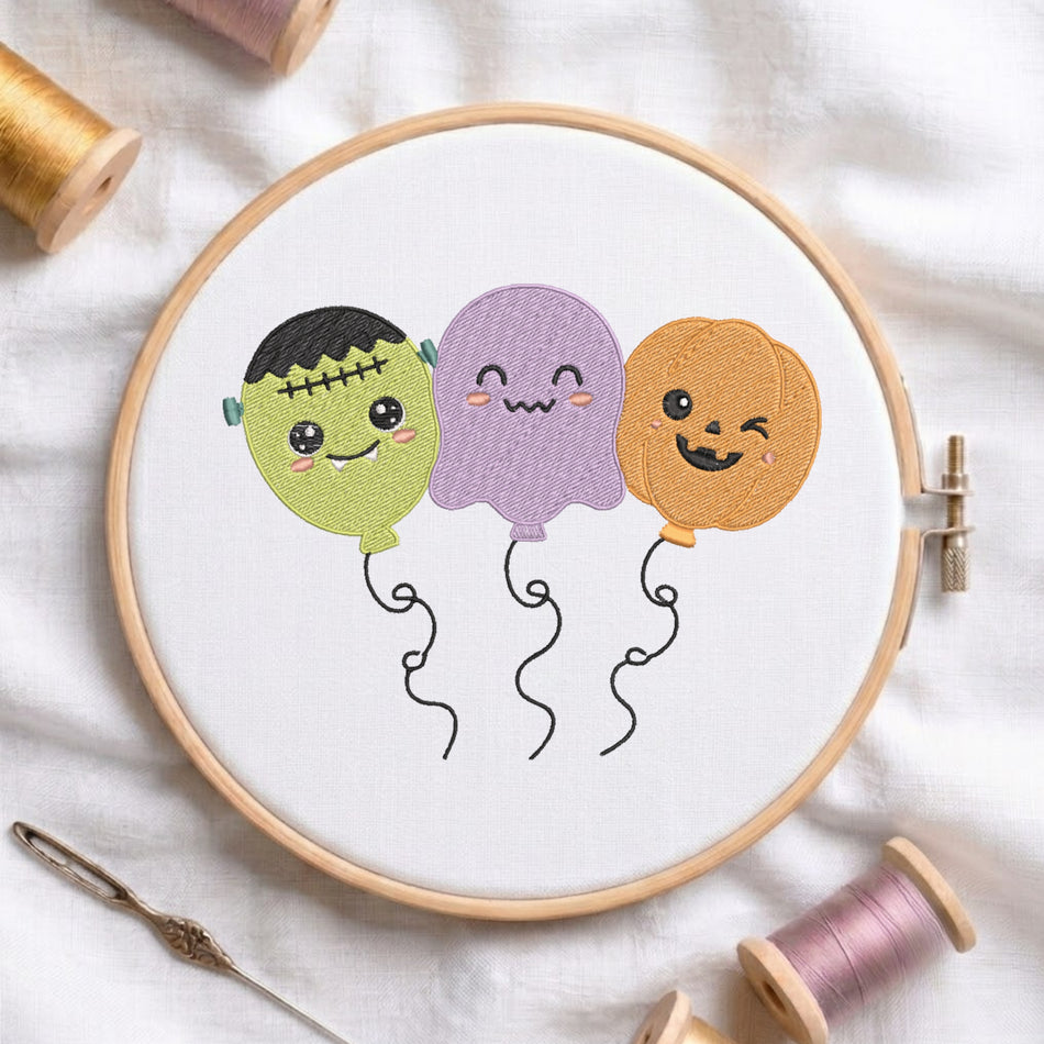 Kawaii Halloween balloons embroidery design inside a wooden hoop showing Frankenstein monster, ghost, and pumpkin character balloons.