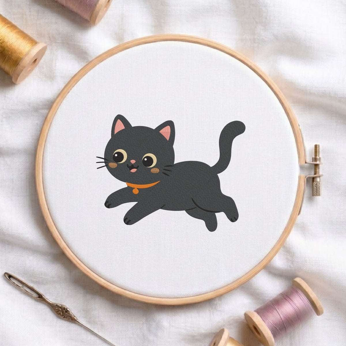 Cute playful black cat with orange collar running Halloween machine embroidery design shown in a wooden embroidery hoop on white fabric with thread spools and a needle