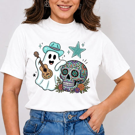 A person wearing a white t-shirt featuring an illustration of a ghost in a teal cowboy hat playing a guitar next to a decorated Day of the Dead sugar skull and a teal star.
