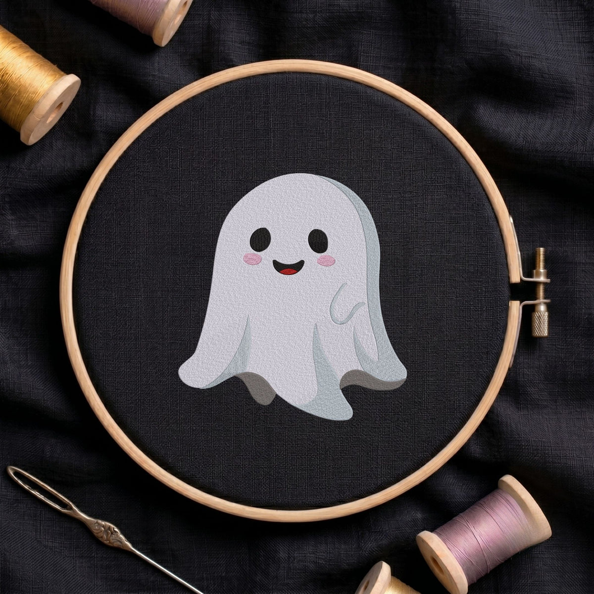 Cute smiling ghost machine embroidery design shown in a wooden embroidery hoop on black fabric with thread spools and a needle   