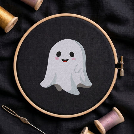 Cute smiling ghost machine embroidery design shown in a wooden embroidery hoop on black fabric with thread spools and a needle   
