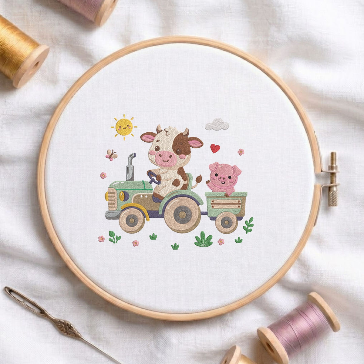 Cute cow driving a tractor with a pig in a wagon machine embroidery design displayed in a wooden hoop on white fabric with thread spools and a needle   
