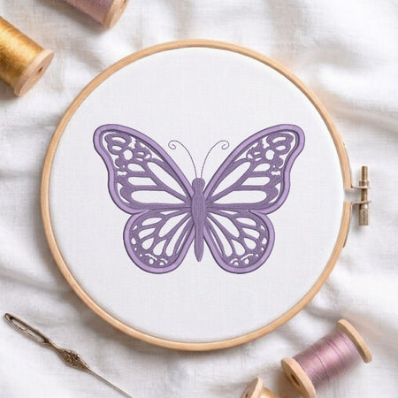 A butterfly embroidery design in lavender purple shown inside a wooden embroidery hoop on white fabric, surrounded by spools of thread and a needle.