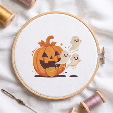 Cute jack-o'-lantern pumpkin with playful flying little ghosts machine embroidery design, displayed inside a round wooden hoop on white fabric with thread spools and a needle.
