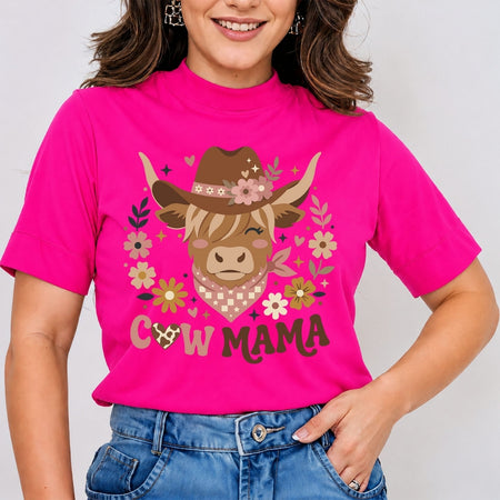 A woman wearing a bright pink short-sleeve t-shirt with a graphic of a cowgirl highland cow and the text 'COW MAMA' in front of blue jeans.