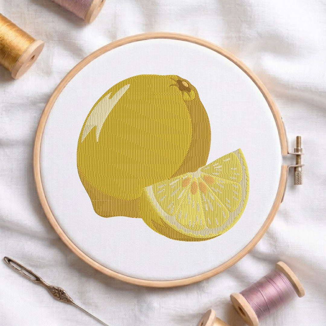 The lemon embroidery design centered in a wooden embroidery hoop, displayed with embroidery thread spools and a needle on a white fabric background.