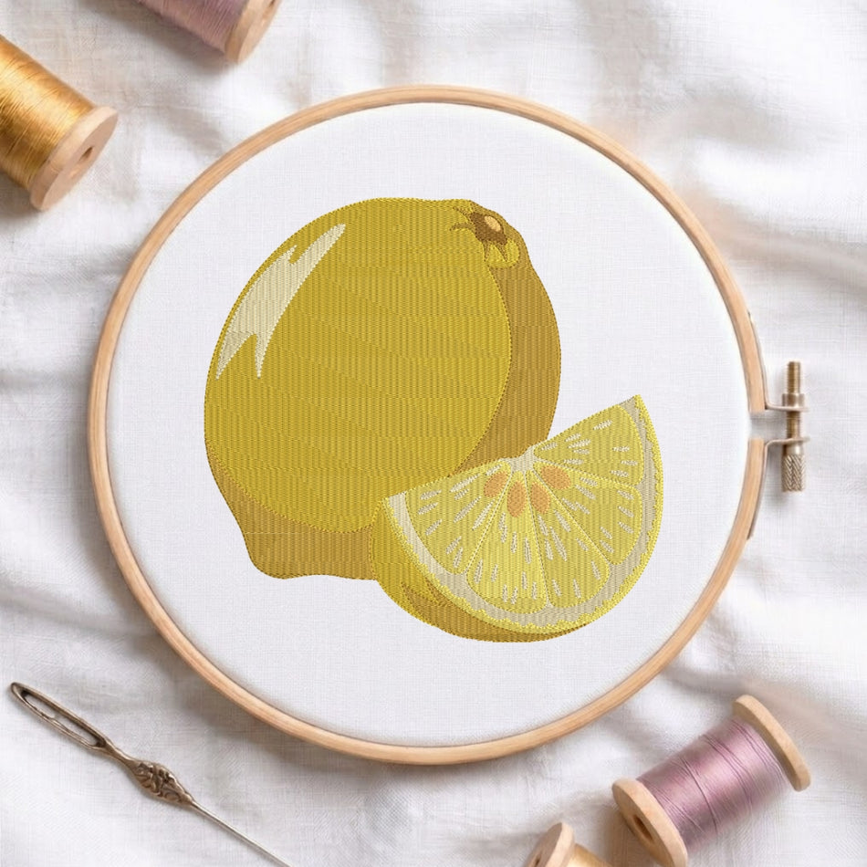 The lemon embroidery design centered in a wooden embroidery hoop, displayed with embroidery thread spools and a needle on a white fabric background.