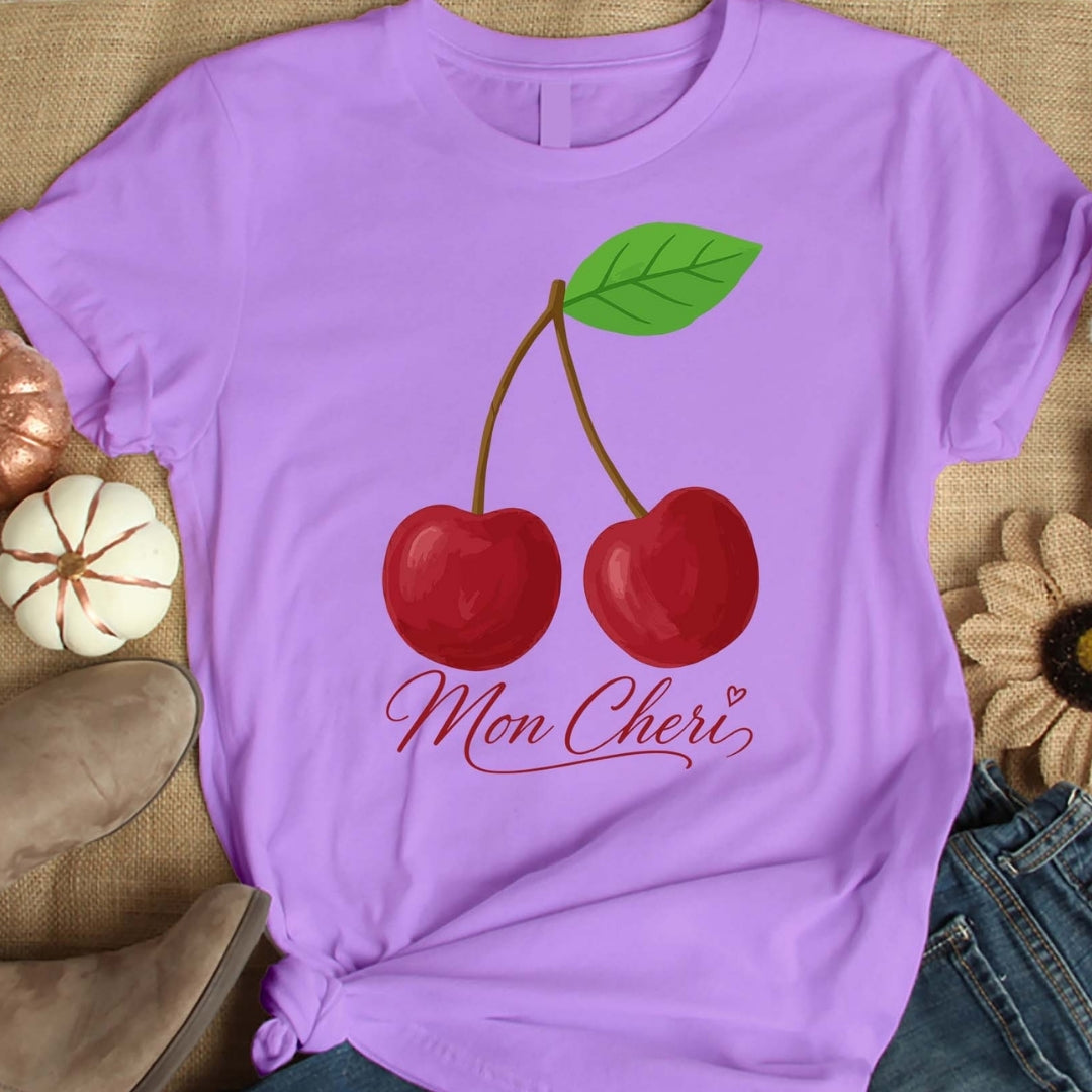 Purple t-shirt with cherry design and 'Mon Cheri' text on a textured surface.