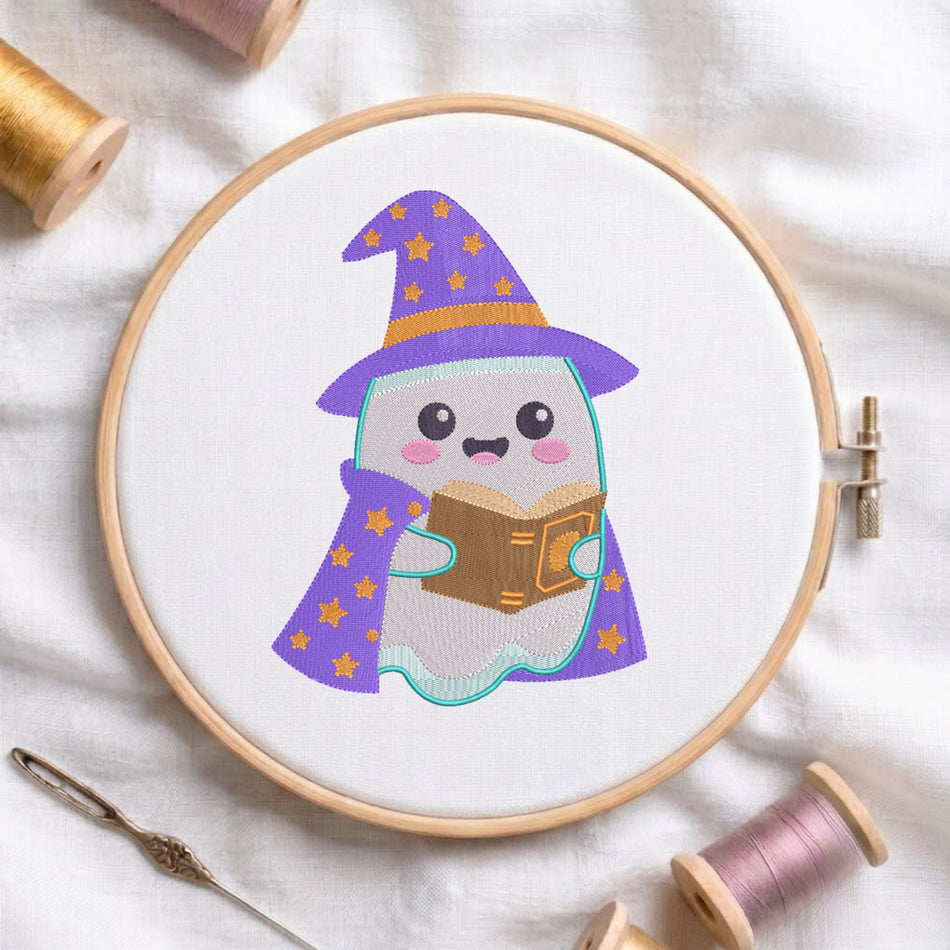 A circular embroidery hoop holding white fabric with a cute embroidered ghost character wearing a purple witch hat and matching cape with gold stars, reading a brown book. The hoop is styled on a white fabric background with spools of thread and a needle nearby.
