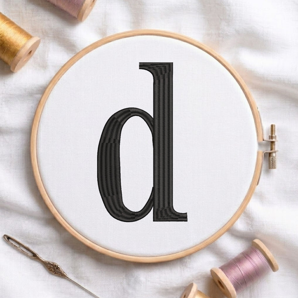 A wooden embroidery hoop holding white fabric with a large black letter 'd' stitched in the center. The hoop is styled on a white fabric background with spools of thread and a needle nearby.