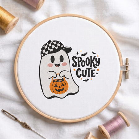 "Spooky Cute" ghost wearing a checkered baseball cap and holding a pumpkin candy bucket machine embroidery design shown in a wooden embroidery hoop on white fabric with thread spools and a needle
