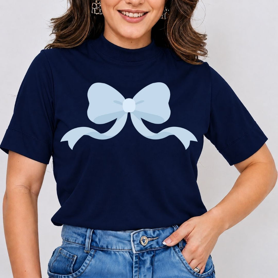 A woman wearing a navy blue mock neck t-shirt with a light blue bow graphic on the front, paired with blue jeans.