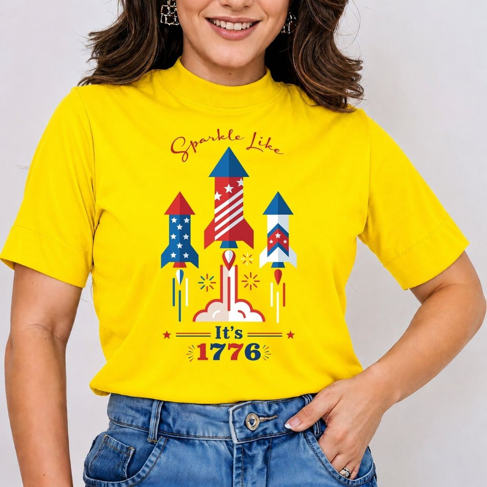 A smiling woman wearing a bright yellow mock-neck t-shirt featuring a large 4th of July firework rocket sublimation design printed on the front.