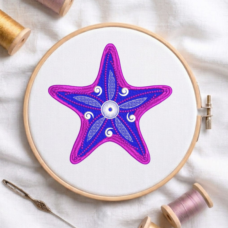 A circular embroidery hoop holding white fabric with a colorful starfish design in purple and blue, surrounded by spools of thread and a needle on a white fabric background.