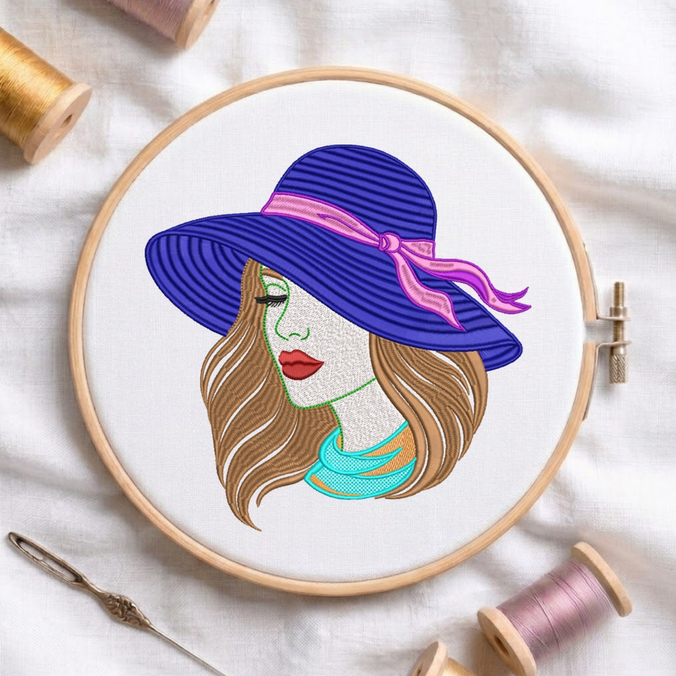 A circular embroidery hoop on white fabric, featuring a stylized illustration of a woman in profile wearing a large blue striped hat with a pink ribbon and a turquoise scarf. Spools of thread and a needle are arranged around the hoop.