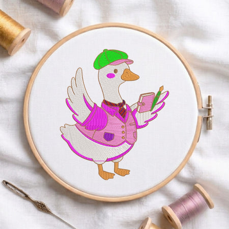 An embroidered design of a duck wearing a green cap, a pink vest, and holding a small notebook and pen, displayed inside a wooden embroidery hoop surrounded by sewing tools and thread.