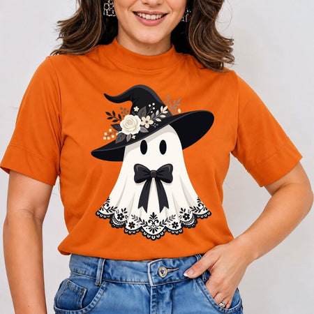 Woman wearing an orange t-shirt featuring a cute ghost design with a witch hat, floral details, and a bow.