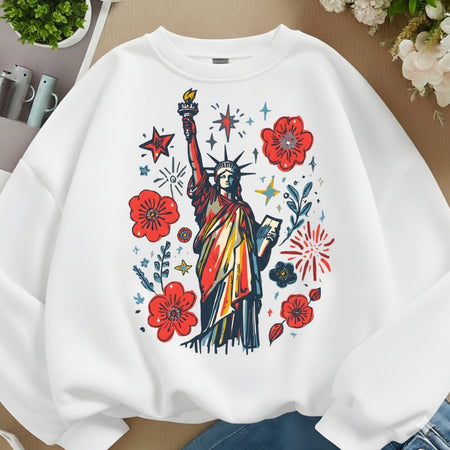 White sweatshirt with colorful graphic of the Statue of Liberty and flowers on a wooden surface.