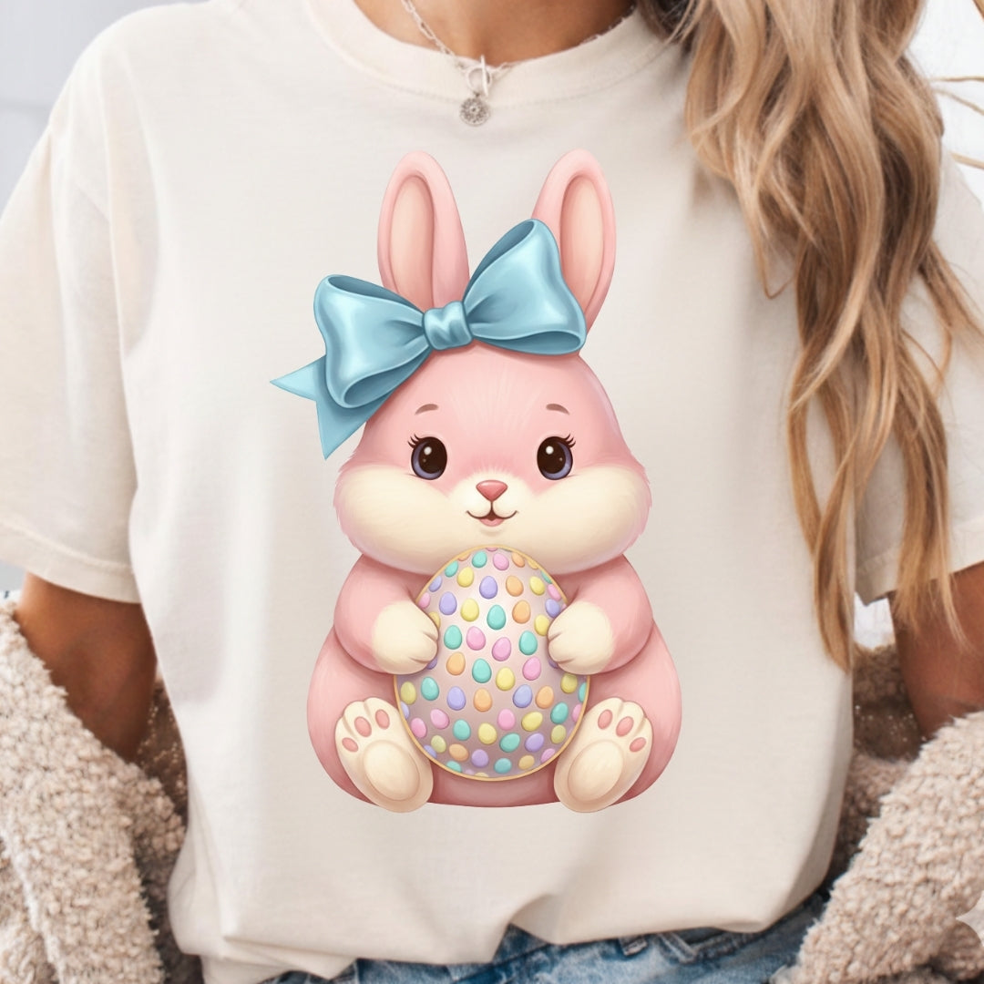 White shirt with a pink bunny design wearing a blue bow and holding a colorful egg.